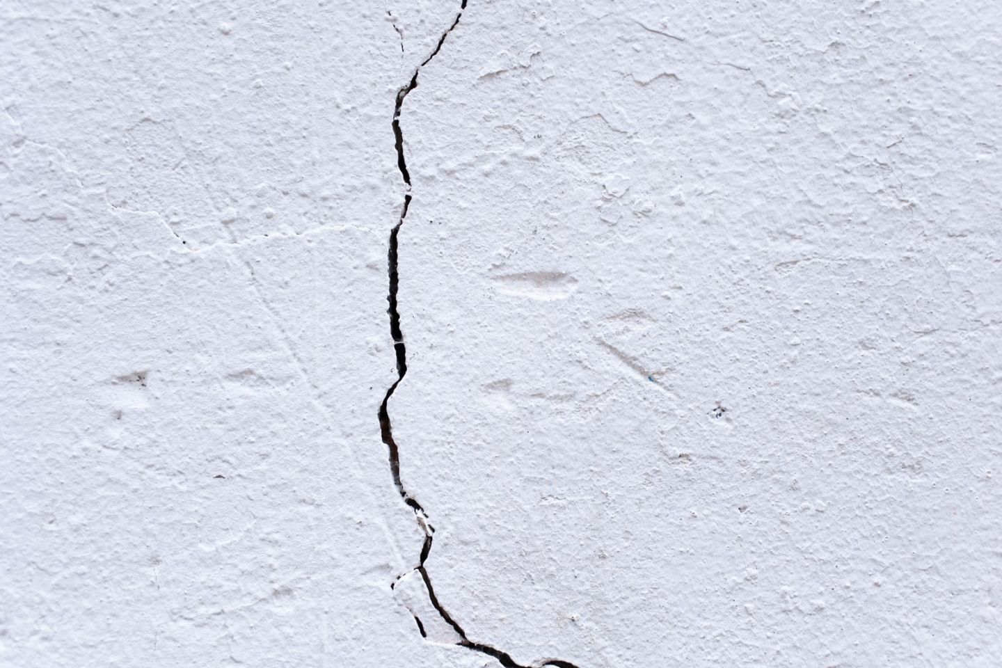 Weiße Putzfläche mit einem durchgehenden, fein verzweigten senkrechten Riss.